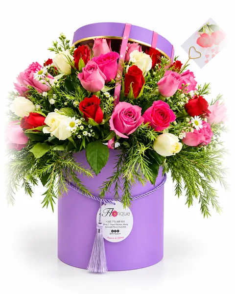Mixed red, pink and ivory roses with daisies overflowing a lilac hatbox